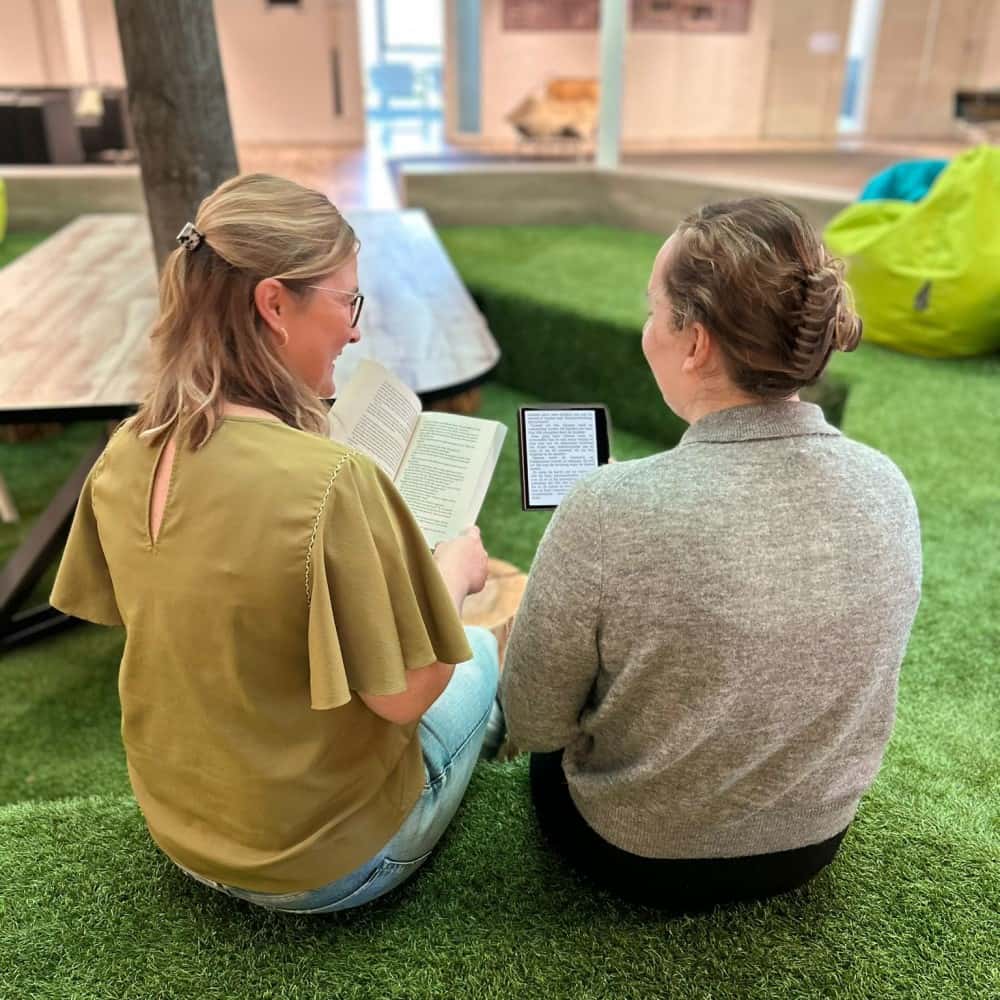 Two readers side by side, one with a printed book and one with an e-reader